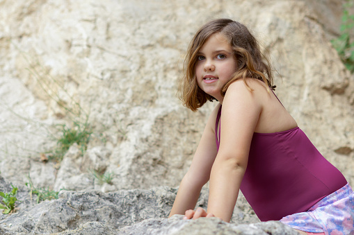 pretty eight-year-old girl in swimsuit sitting on the rocks of a river bank