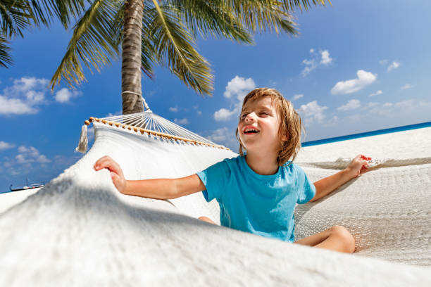 Happy little boy sitting in hammock during summer day on the beach.