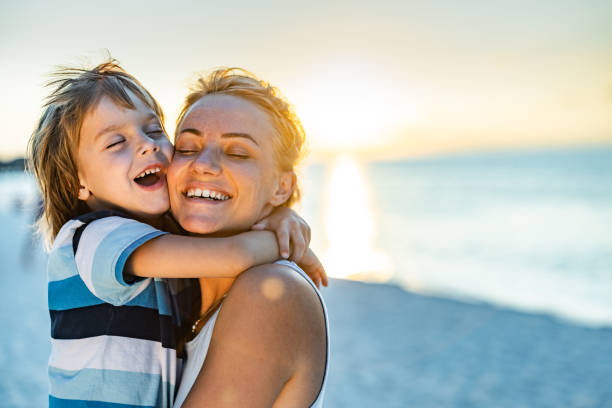 Loving single mother and son embracing on the beach at sunset.