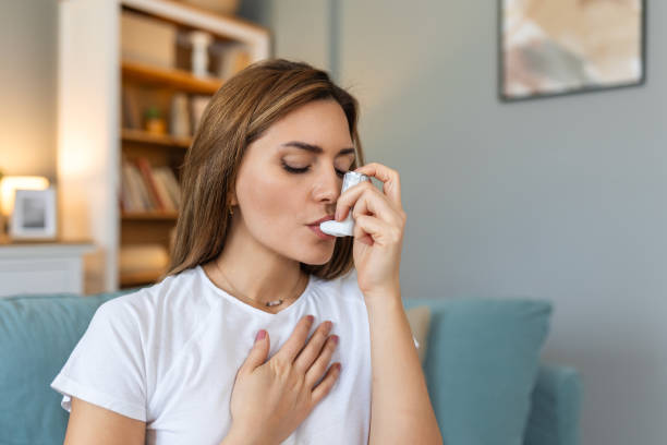 istock Woman using inhaler while suffering from asthma at home. Young woman using asthma inhaler. Close-up of a young woman using asthma inhaler at home. 2150789635