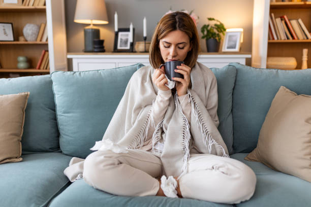 istock Sickness, seasonal virus problem concept. Woman being sick having flu drinking tea on sofa. Sick woman lying in bed with high fever. Cold flu and migraine. 2150789684