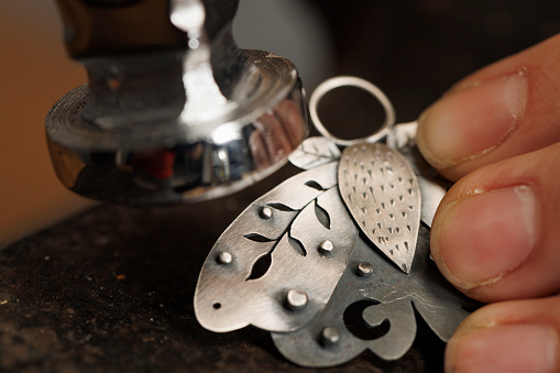 Jeweler craft workshop  A beautiful young woman  jeweler,  produces hand made  a Locket, butterfly  pendant, uses metal hammer.  Vintage and modern jeweler tools  Work Hand Tool  DIY. Small business