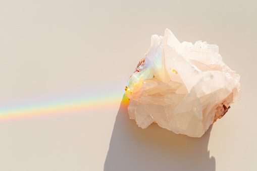 Quartz Prism's Rainbow Reflection at sunlight, close up of clear quartz crystal captures prismatic rainbow, natural facets and beauty of mineral. Minimal aesthetic nature pattern, beige pastel color