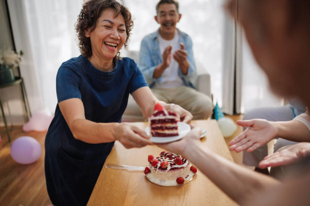 A smiling senior woman serves a birthday cake to her guests.