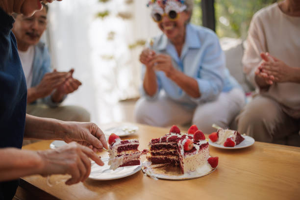 A senior woman serves a birthday cake to her guests.