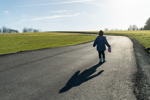 Little girl walking on a road in the countryside with a shadow on the road