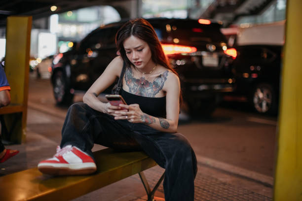 Alternative young woman is using her phone in the city at night.
