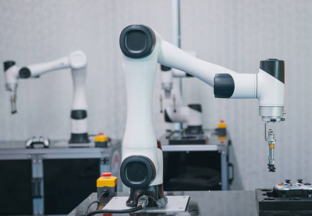 A robot is working on a piece of machinery. The robot is white and black. The robot is in a room with other robots