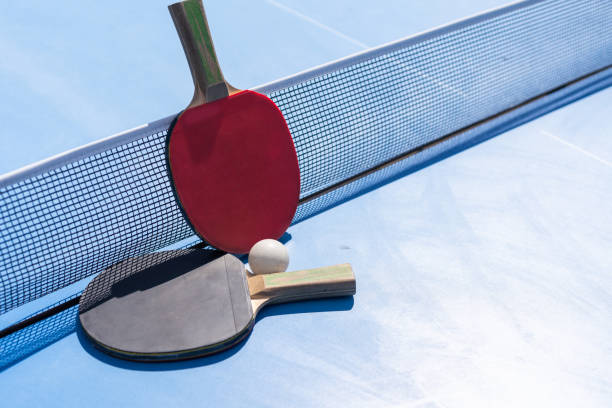 istock Two table tennis or ping pong rackets and ball on blue table with net 2150805739