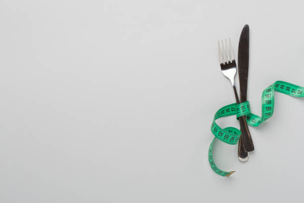 istock Knife and fork wrapped in tape measure on color background, top view 2150806094