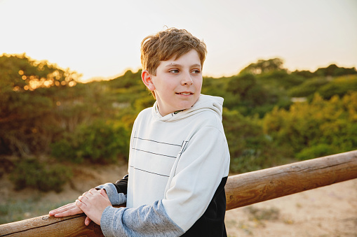 Happy cheerful teenager standing on beach at sunset. happy preteen boy smiling at the camera. Kid on family vacation at the sea