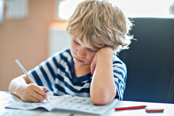 istock Portrait of tired upset boy doing homework in kitchen at home. Elementary school studing writing and learning. Sad and angry child. 2150808233