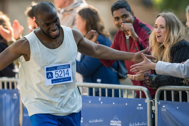 istock Marathon Audience Clapping and Cheering Their Loved Ones Participating in the Race: Black Athletic Male Marathon Runner Giving a High Five to Female Friend Supporting Him in the Audience While Running 2150808370