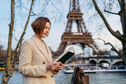 Beautiful young woman reading a book in front of an Eiffel Tower in Paris in France.