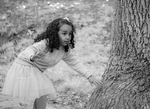 Girl looking away while standing by tree trunk