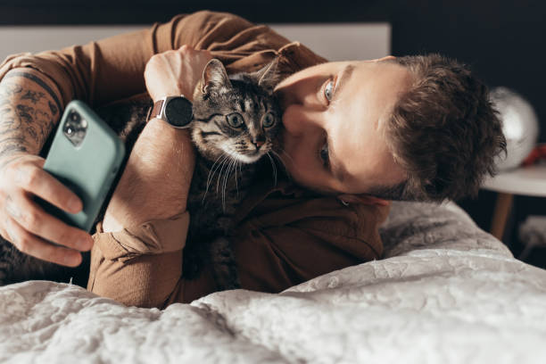 Man laying at the bed with his cat and making selfie