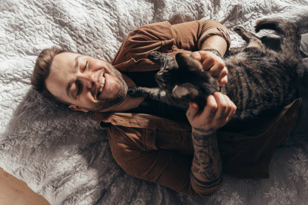 istock Man laughing and stroking his striped cat while spending time with him at bedroom 2150817297