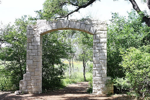 A picture of a stone archway nestled among trees with a dirt path leading through it.