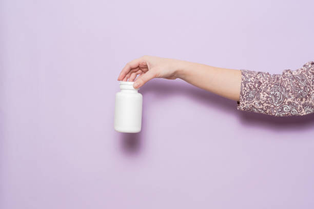 istock White plastic bottle in female hand in lilac background. Packaging for pills, capsules or supplements. 2150818357