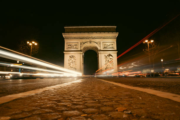 The iconic Arc de Triomphe in Paris beautifully lit against the night sky, with motion blur from passing cars capturing the lively atmosphere of the city.