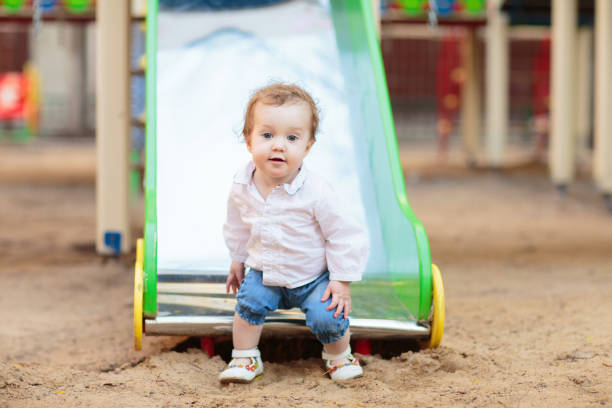 Child playing on playground on sunny summer day in a park. Kids swing and slide. School or kindergarten yard and play ground. Summer outdoor activity. Kid playing.