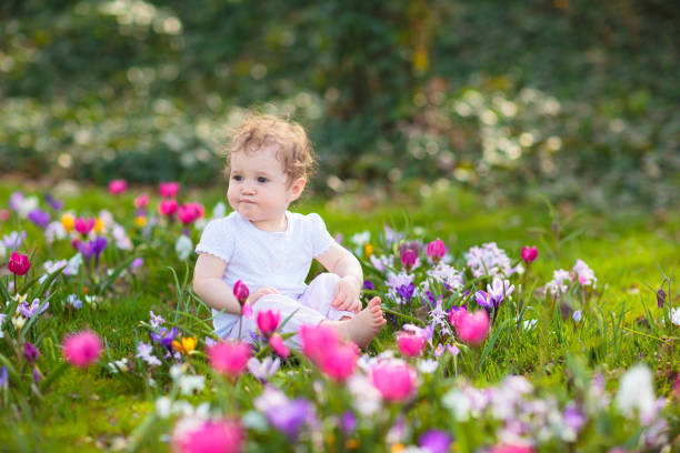 Cute little girl in pink dress playing in blooming spring park with first white wild anemone flowers. Child on Easter egg hunt in blooming garden. Kids play outdoor picking flower bouquet.