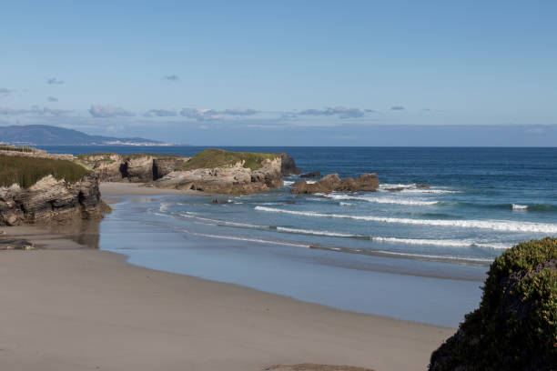 istock A tranquil beach with rocky formations, gentle waves, clear skies, and distant mountains, exuding calmness and natural beauty. 2150823472