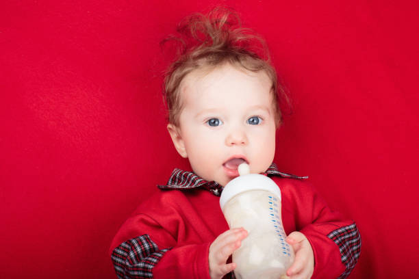 cute asian baby sitting on bed drinking milk from kids bottle
