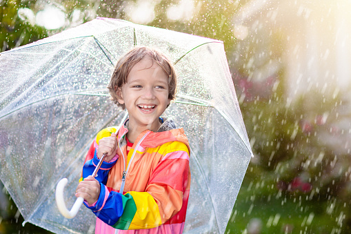 Child playing in autumn rain. Kid with umbrella. Little boy running in a park in fall season. Outdoor fun for kids by any weather. Rain waterproof wear, boots and jacket for children.