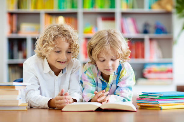 Shot of two adorable brothers reading books while relaxing together on the sofa at home