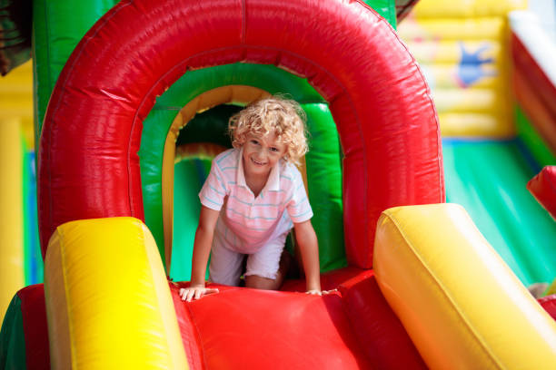 Child jumping on colorful playground trampoline. Kids jump in inflatable bounce castle on kindergarten birthday party Activity and play center for young child. Little boy playing outdoors in summer.