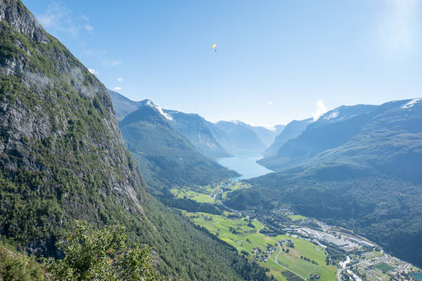 The expansive view of a majestic fjord, with mountains flanking the shimmering blue waters that stretch into the distance. The sunlight filters through the peaks, casting shadows and illuminating the lush green valleys below.