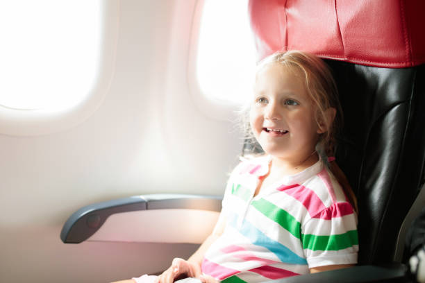 Child in airplane. Kid in air plane sitting in window seat. Flight entertainment for kids. Traveling with young children. Kids fly and travel. Family summer vacation. Little girl with toy in airplane.