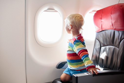 Child in airplane. Kid in air plane sitting in window seat. Flight entertainment for kids. Traveling with young children. Kids fly and travel. Family summer vacation. Little boy with toy in airplane.