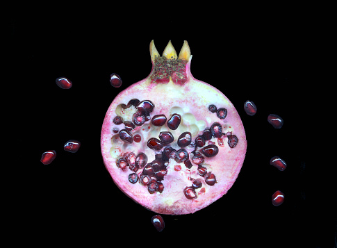 A piece of pomegranate with scattered grains and pomegranate leaves, isolated on a white background