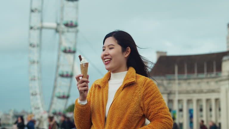 Asian woman eating ice cream with positive emotion while traveling at Westminster Bridge Center city in London, United Kingdom