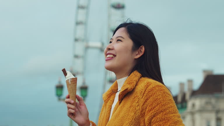 Asian woman walking and eating ice cream with positive emotion while traveling at Westminster Bridge Center city in London, United Kingdom