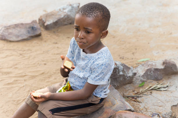 african village ,child snacking on biscuits and maize snacks sited on a stone in the yard