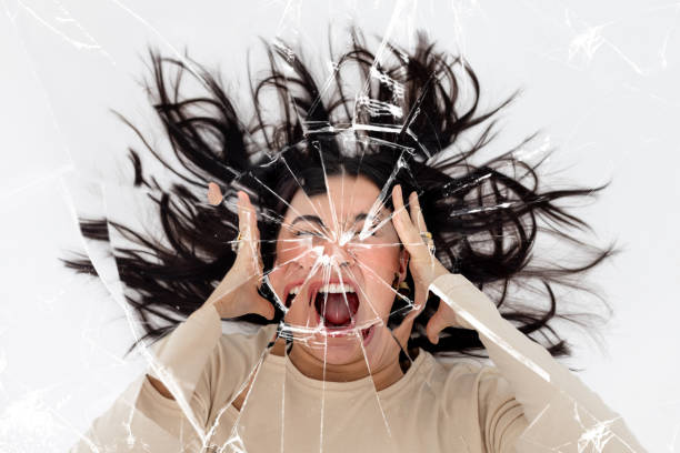 Breaking the Mirror with a Scream Woman screaming with her hands either side of her head with a cracked mirror effect over the image. furious stock pictures, royalty-free photos & images