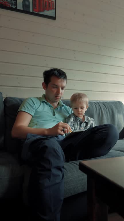Vertical of Curious toddler watches father drawing images in notepad