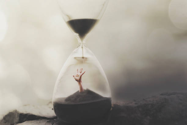hand emerging from the sand inside an hourglass, concept of time