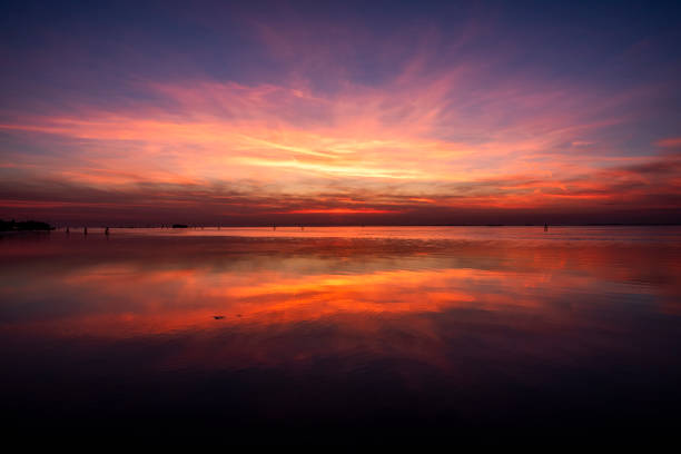 fiery sunset with red and orange colors is reflected on the calm waters of the Venetian lagoon with bricole and trees photographed from the Lido of Venice in Veneto Italy