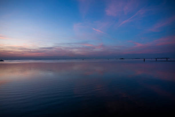 fiery sunset with red and orange colors is reflected on the calm waters of the Venetian lagoon with bricole and trees photographed from the Lido of Venice in Veneto Italy