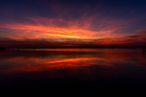 fiery sunset with red and orange colors is reflected on the calm waters of the Venetian lagoon with bricole and trees photographed from the Lido of Venice in Veneto Italy