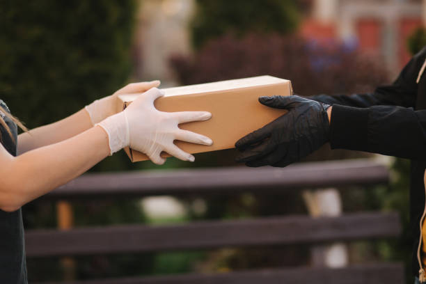 Close-up hands in protective gloves hold parcel. Delivery dervise bring order to customer. Online shopping concept. Black and white gloves. High quality photo