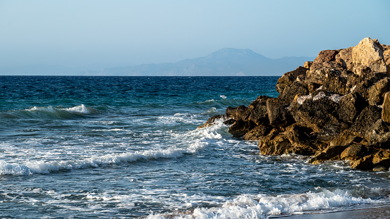 Mesmerizing landscape with the sea in which waves rage and crash against stone breakwaters, with mountains visible in the distance.