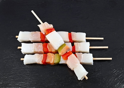 Raw fish skewers with peppers on black slate cutting board. Top view.