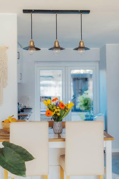 istock Stylish and modern boho, scandi interior of open space white kitchen with multicolor various flower in vase on kitchen counter table, macrame and industrial style ceiling lamps. Design home decor 2150852670