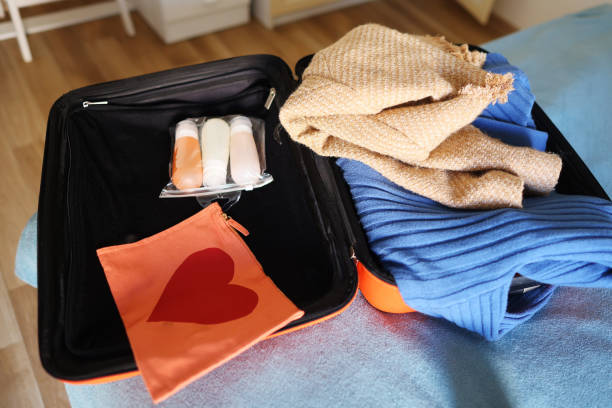 istock Open orange suitcase with different clothes packed for journey at home 2150853750