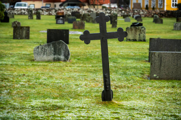 A stone cross rests on a sturdy pedestal in front of a rustic wall. Nature surrounds the structure, creating a peaceful and reflective atmosphere in this historic location.
